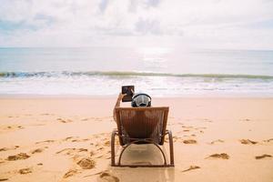 hombre haciendo una videollamada en vacaciones de verano. hombre latinoamericano sentado en la silla de playa con auriculares y una tableta foto