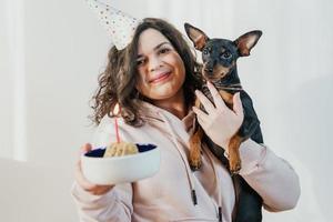 Happy young girl giving homemade cake to her dog, indoors photo