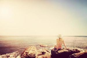 Young woman sunbathing on rocky beach. Vintage mood photo