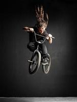 joven con rastas saltando en su bicicleta bmx. foto