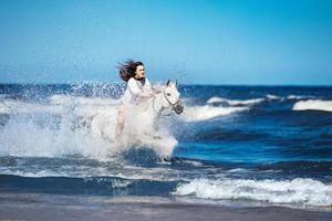 niña en un caballo blanco asaltando el agua foto