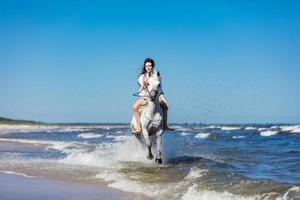 chica galopando sobre un caballo blanco en el mar foto