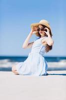 A girl in straw hat sitting on a beach by the sea photo