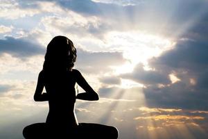 una silueta de una mujer sentada en posición de yoga, meditando contra el cielo del atardecer. foto