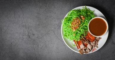 Jade noodle Asian Thailand food , roasted duck with jade noodle on white plate and duck sauce on black background, green noodles Chinese food - top view photo