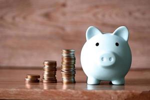 Stack coins and piggy bank on wooden background, blue piggy bank saving money for education study or investment concept photo