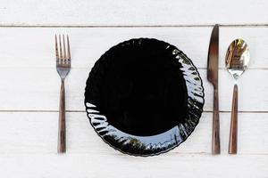 Colocar comida en la mesa con un juego de platos negros en la mesa, cena, plato vacío, cuchara, tenedor y cuchillo en la mesa de madera, vista superior foto