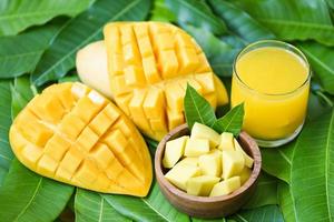 mangos maduros dulces - vaso de jugo de mango con rebanada de mango en hojas de mango del concepto de fruta de verano tropical de árbol foto