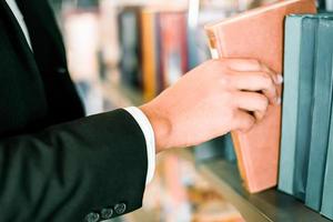 Business man or student holding a book on hand or Picking a book on bookshelf in the library bookshelves background - Business Education Study Concept photo