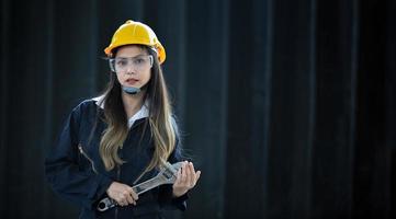 retrato de un hermoso ingeniero asiático sosteniendo una llave inglesa el fondo es un contenedor, concepto de ingeniero o mecánico industrial. foto