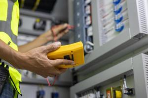 probador de trabajo de ingeniero electricista que mide el voltaje y la corriente de la línea eléctrica en el control del gabinete eléctrico. foto