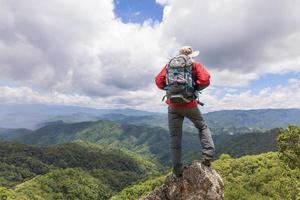 Young happy woman with backpack standing on a rock  and looking to a valley below photo