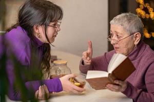 grandmother and granddaughter drink tea sitting at the table and read a book. photo
