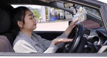 Desperate beautiful Asian woman holds cash dollar bills sitting inside her car at a gas station photo