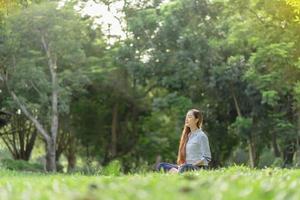 Happy woman doing meditation and relaxing in the park. Meditation in nature. Concept of healthy lifestyle and relaxation. Pretty woman practicing meditation on the grass