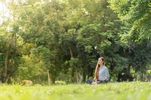 Happy woman doing meditation and relaxing in the park. Meditation in nature. Concept of healthy lifestyle and relaxation. photo