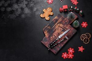 Christmas homemade gingerbread cookies, spices and cutting board on dark background photo