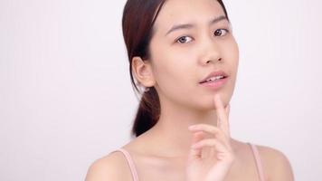 rallentatore della ragazza asiatica con trucco naturale che osserva alla macchina fotografica e accarezza delicatamente il viso su priorità bassa bianca. video