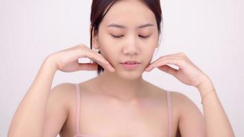 Slow motion of Asian girl with natural make up looking to camera and patting her face gently on white background. video