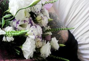 White flowers, bouquet on a white sheet, black leg tattoo photo