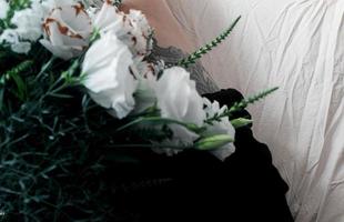 White flowers, bouquet on a white sheet, black leg tattoo photo