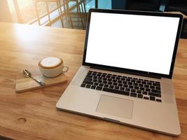 computadora portátil de pantalla blanca vacía para información y taza de café en la mesa de madera en la cafetería. concepto de negocio. copiar espacio para texto foto