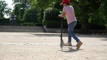een jongenskind rijdt op een scooter in een zomerpark, dag video