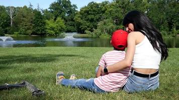 madre e hijo sentados juntos pacíficamente en la hierba verde, familia cerca del lago, día de verano video