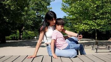 la joven madre con su hijo pequeño hace una foto selfie con un teléfono inteligente en un parque video