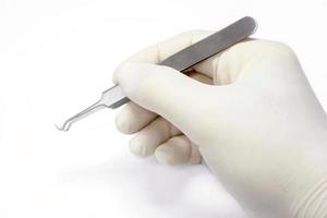 Hand of doctor in a white medical latex glove holding a blackhead forceps remover and showing the gesture of holding the forceps isolate on white background and make with photo