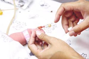 The nurse hands is stabbing injection plug with use a medical tape to attach the needle to the baby's hand and wounding. photo