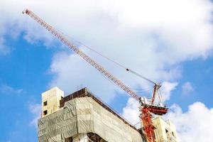 Building under construction with hoisting cranes on bright blue sky background photo