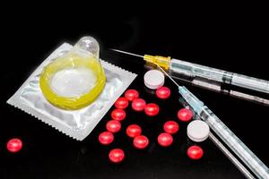 White and red medicines with a plastic syringe and condom isolate on black background. Sample of what caused the HIV infection. and The condom is to prevent infection. photo