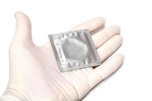 Condom in package put on doctor hand in medical latex glove on white background. photo