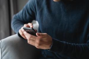 Happy Asian man using smartphone on sofa in living room at home, searching data and social media on internet. photo