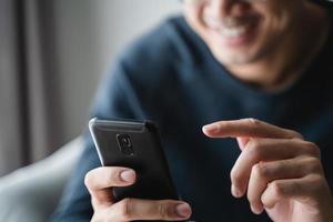 Happy Asian man using smartphone on sofa in living room at home, searching data and social media on internet. photo