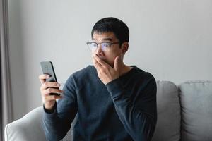 retrato de un hombre asiático emocionado mirando el teléfono móvil, un hombre que recibe buenas noticias usando un teléfono inteligente en casa. foto