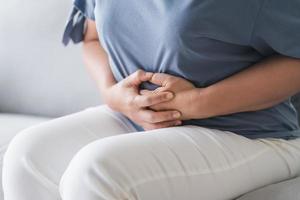 mujer que sufre de dolor de estómago sentada en el sofá de casa. dolor abdominal, gastritis, regla, menstruación. foto