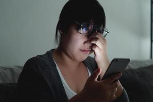 stressed woman take off glasses massage eyes feel fatigue suffering from headache, exhausted woman having eyestrain using smartphone in dark living room at night. photo