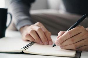 left handed man writes in a notebook on the table photo