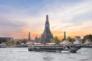 The Temple of Dawn, Wat Arun, on the Chao Phraya river with passenger ships or boat and a beautiful sky in twilight time at Bangkok, Thailand photo