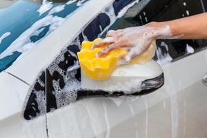 mano de mujer con esponja amarilla lavando espejo lateral coche moderno o limpiando automóvil. concepto de lavado de autos foto