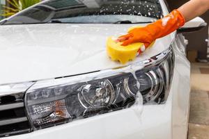 mano de mujer con guantes naranjas con esponja amarilla lavando faros coche moderno o limpiando automóviles. concepto de lavado de autos foto