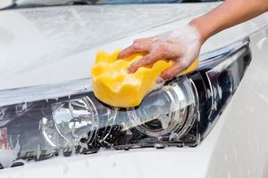 mano de mujer con esponja amarilla lavando faros coche moderno o limpiando automóviles. concepto de lavado de autos foto