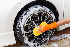 mano de mujer con guantes naranjas con esponja amarilla, rueda de lavado, automóvil moderno o automóvil de limpieza. concepto de lavado de autos foto