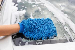 mano de mujer con tela de microfibra azul lavando espejo retrovisor coche moderno o limpiando automóvil. concepto de lavado de autos foto