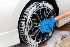 Woman hand with blue microfiber fabric washing wheel modern car or cleaning automobile. Car wash concept photo