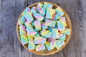 Multi-colored Marshmallow twist in a wooden dish on a wooden background. Copy space background and texture photo