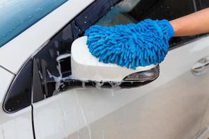 mano de mujer con tela de microfibra azul lavado espejo lateral coche moderno o limpieza de automóviles. concepto de lavado de autos foto