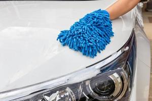 mano de mujer con tela de microfibra azul lavado de faros coche moderno o limpieza de automóviles. concepto de lavado de autos foto